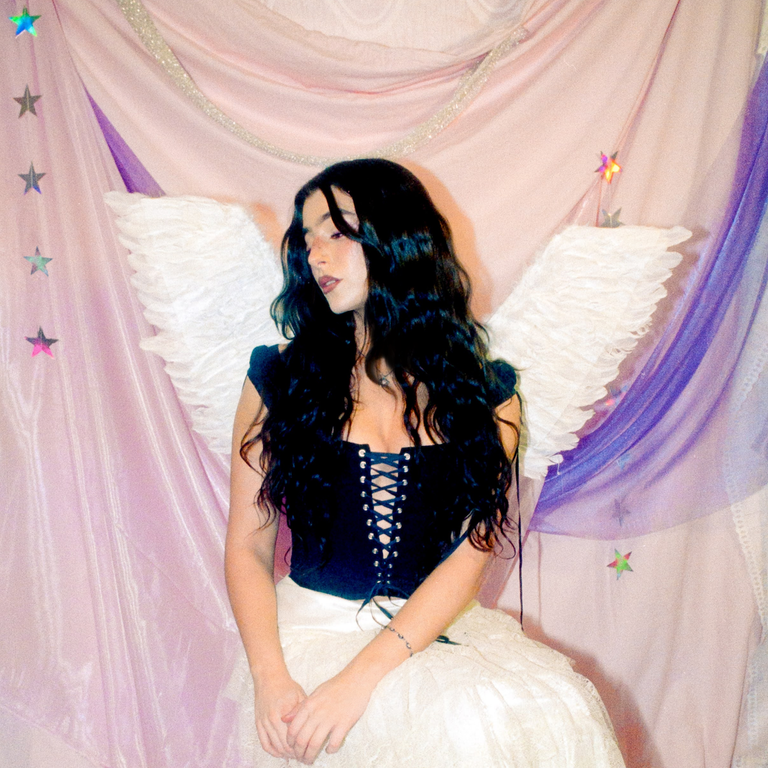 Effie Isobel Libra Rising EP artwork, showing the singer wearing white angel wings and a black corset against a draped pink backdrop.